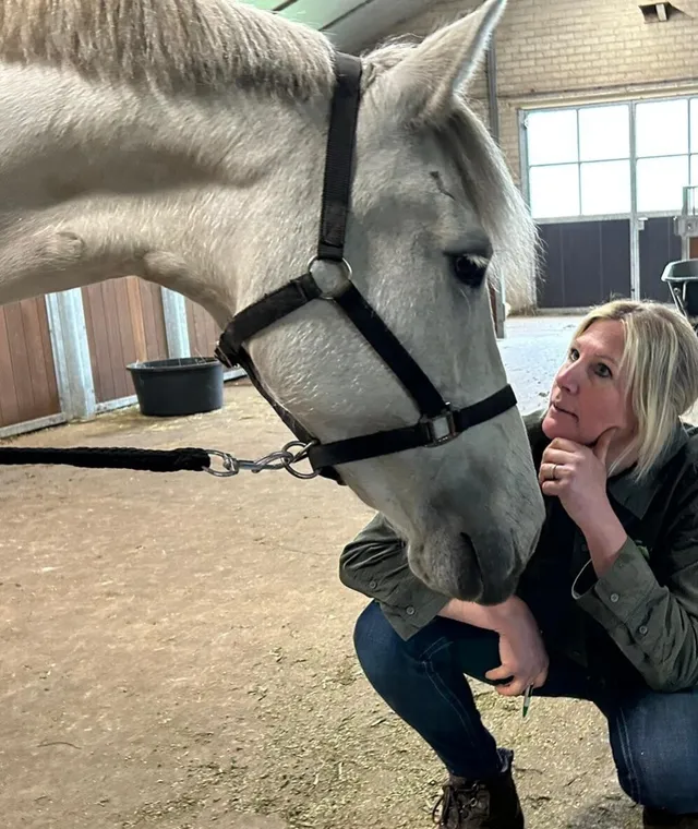 Angelique zit gehurkt bij een witte pony en kijkt haar aandachtig aan